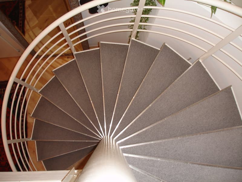 Spiral staircase with gray carpeted steps and white metal railing, wooden flooring visible in the background.