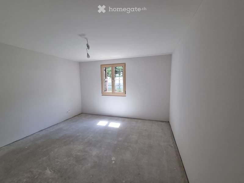 Empty room with bare walls, concrete floor, and a single window with a brown frame. No furniture or equipment present.