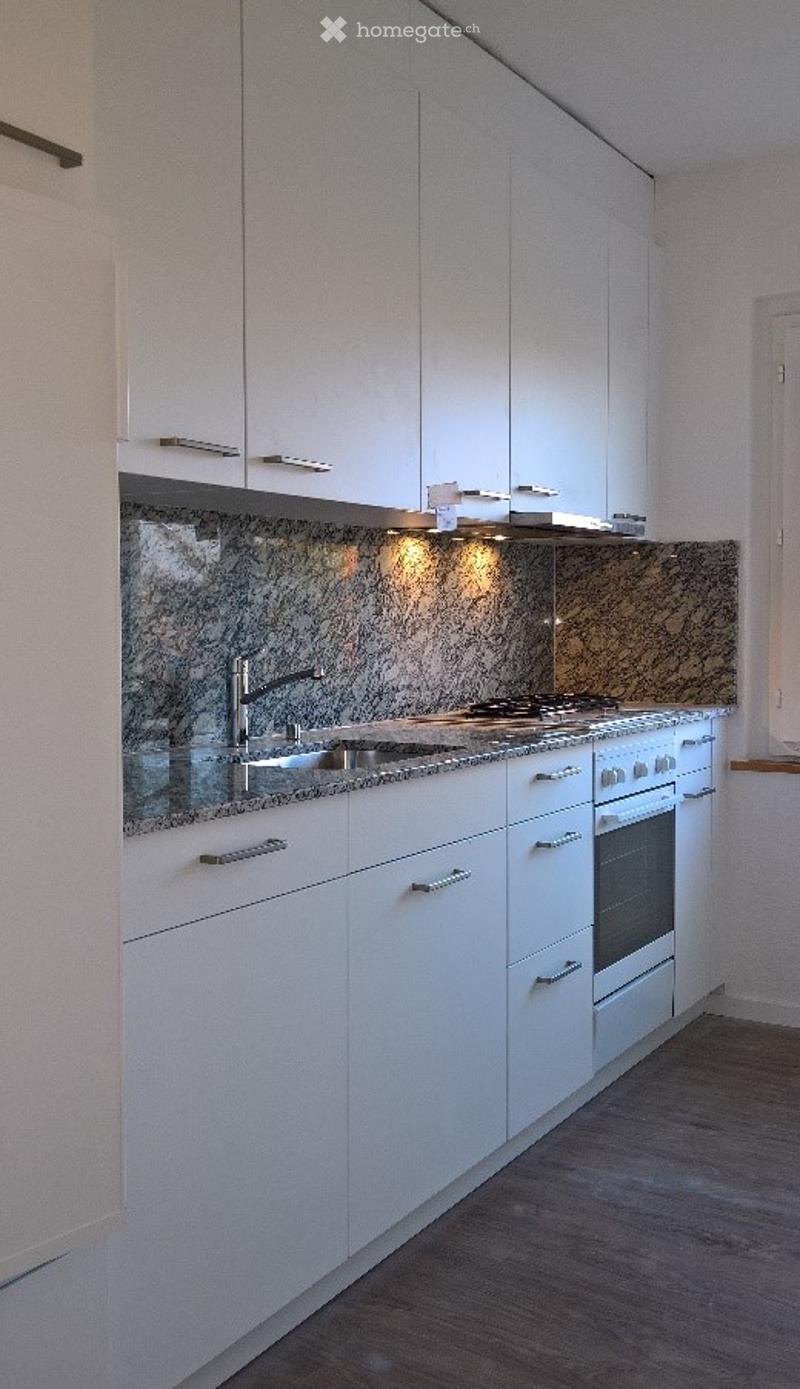 Modern kitchen with white cabinets, granite backsplash, stainless steel sink and stove, and built-in oven.