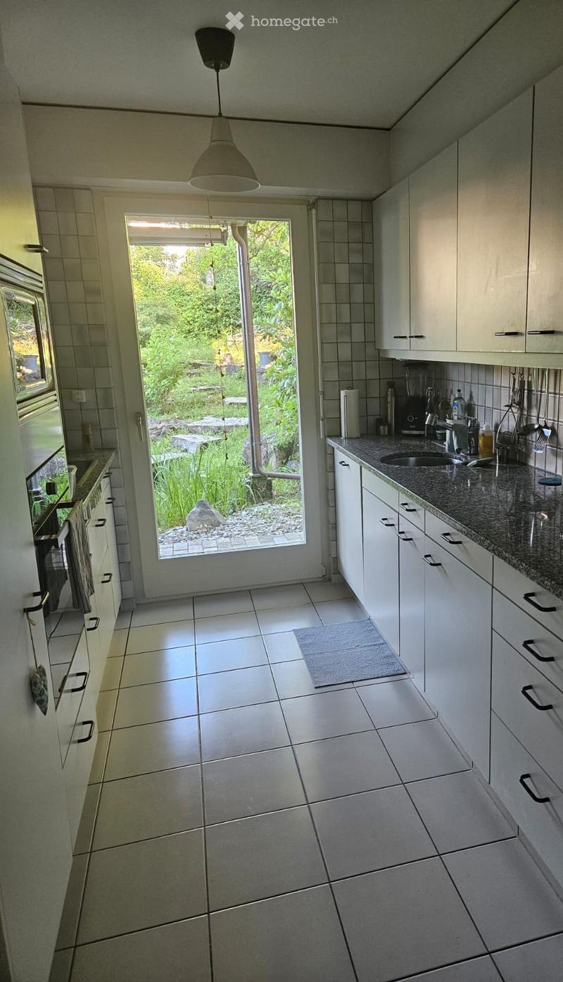 Modern kitchen with white cabinets, granite countertop, and a large window overlooking a garden. Includes a sink, oven, and various appliances.