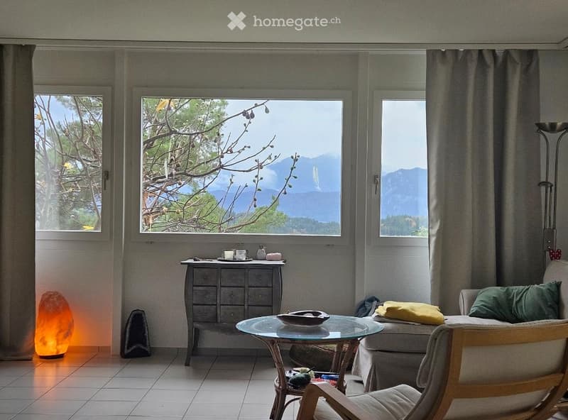 Bright living room with large windows offering a scenic mountain view, featuring a sofa, coffee table, side table, and decorative items.