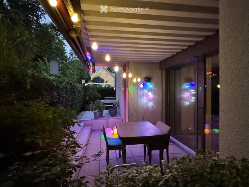 Outdoor patio with a table and chairs, string lights, and potted plants.