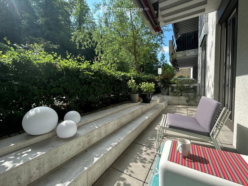 Balcony with a lounge chair, small table, cup, and decorative spherical lamps on a raised concrete platform.