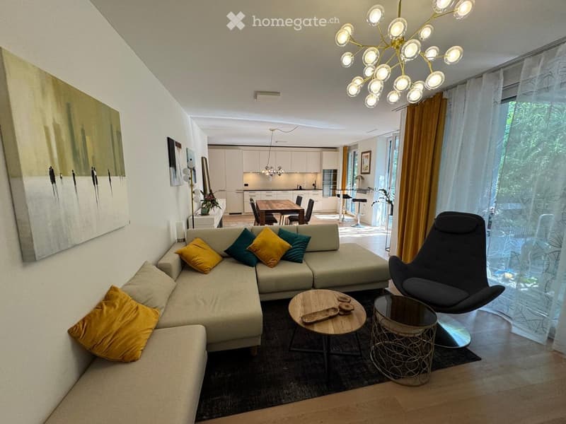 Modern living room with a sectional sofa, colorful throw pillows, a coffee table, a round side table, a modern chair, and a dining area with a table and chairs in the background.