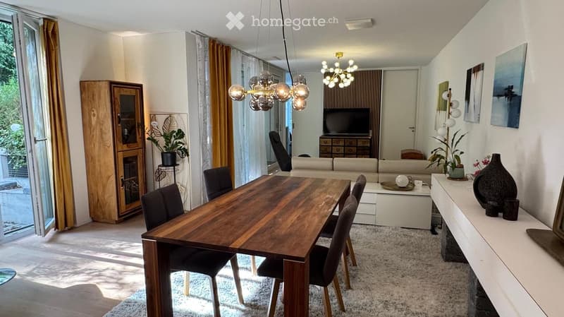 Modern open-plan living and dining area with a wooden dining table, black chairs, a light-colored sofa, a TV, a wooden cabinet, and decorative vases.