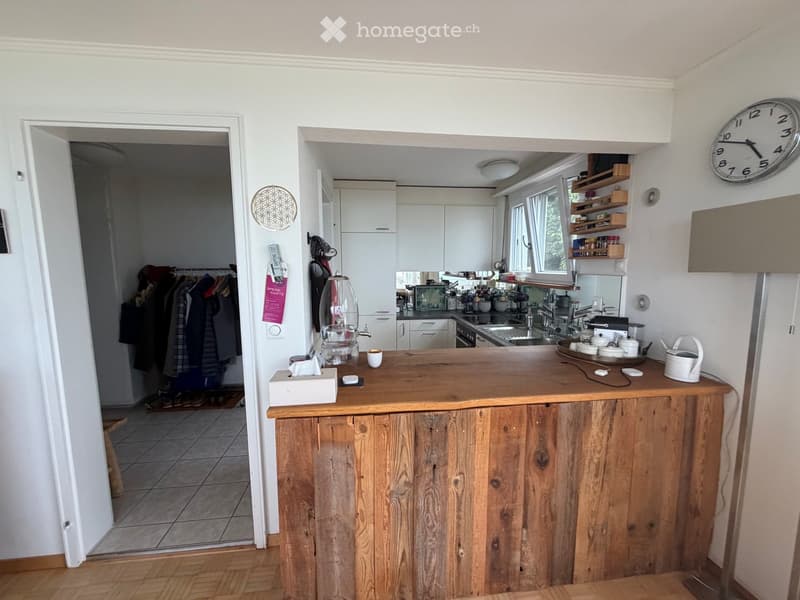 Bright kitchen with wooden island, white cabinets, sink, oven, and various kitchen items on the counter and shelves.