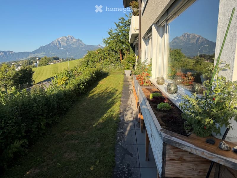 Balcony with wooden planters, lush greenery, and a scenic mountain view in the background.