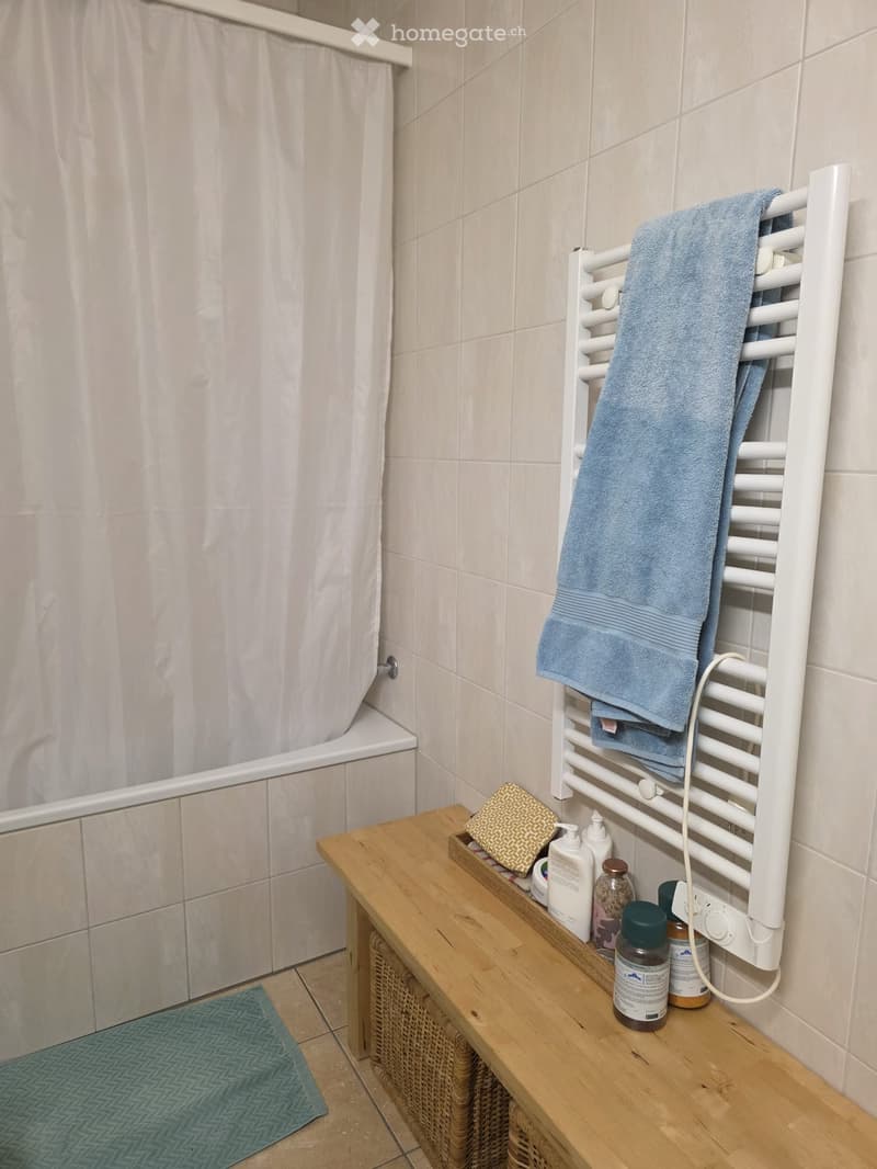 Bathroom with a bathtub, towel rack, wooden bench, and various toiletries.