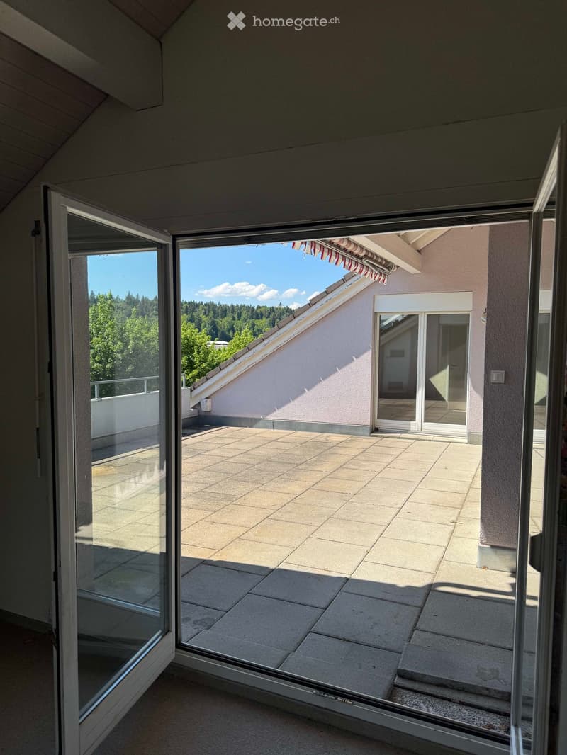 Spacious balcony with tiled flooring, large glass doors, and a view of a green, forested area.