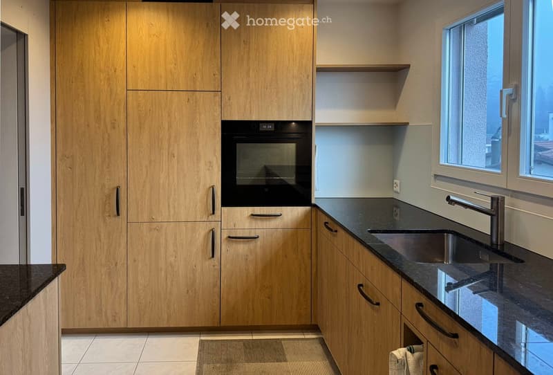 Modern kitchen with light wooden cabinets, black granite countertops, stainless steel sink and faucet, and built-in oven.
