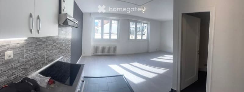 Empty kitchen with white cabinets, a tiled backsplash, and a modern electric stove. The space is unfurnished, with natural light from windows and a radiator visible.