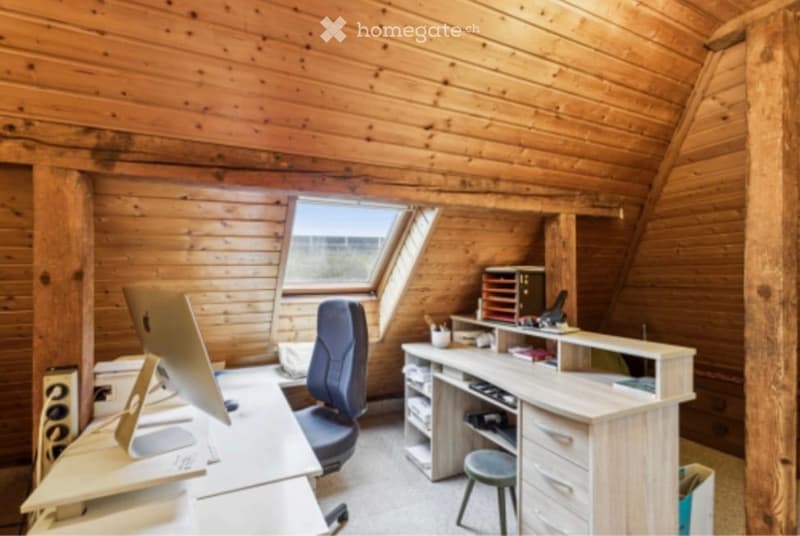 Cozy wooden-paneled room with a large skylight window offering a view, featuring a desk with a computer monitor, a comfortable chair, a small stool, and a cabinet with storage boxes.