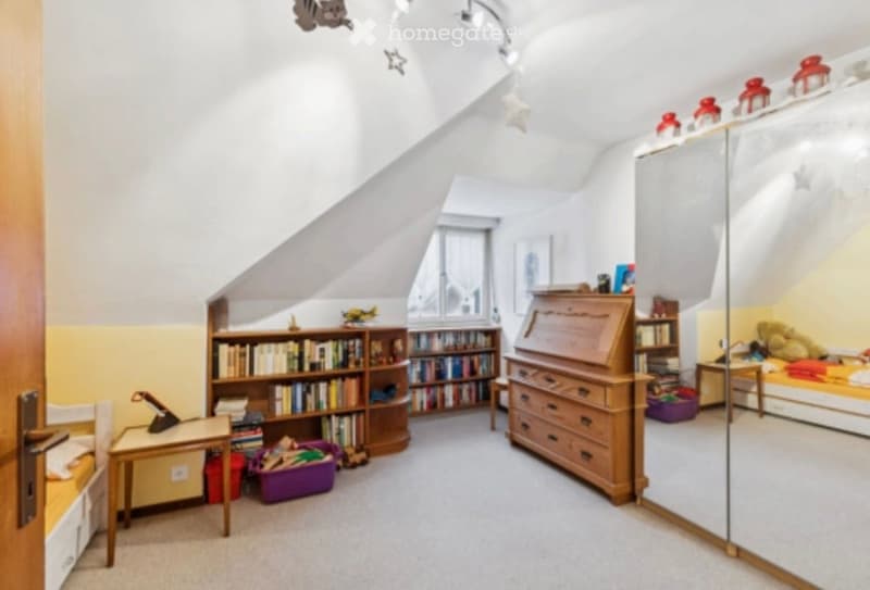 Bright, cozy bedroom with slanted ceilings, large window, bookshelf, desk, bed, and dresser.