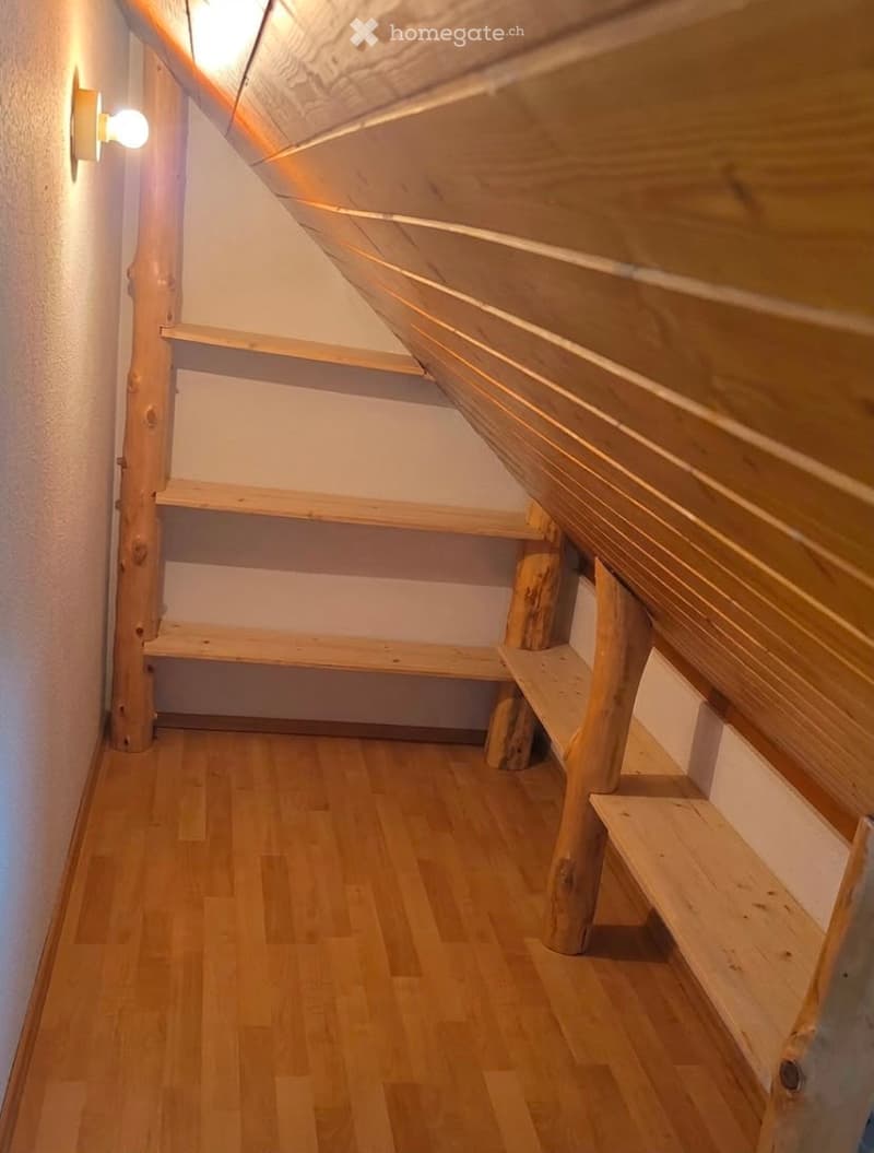 Empty wooden hallway with built-in wooden shelves and a slanted wooden ceiling. The walls are white, and the floor is made of light wooden planks.