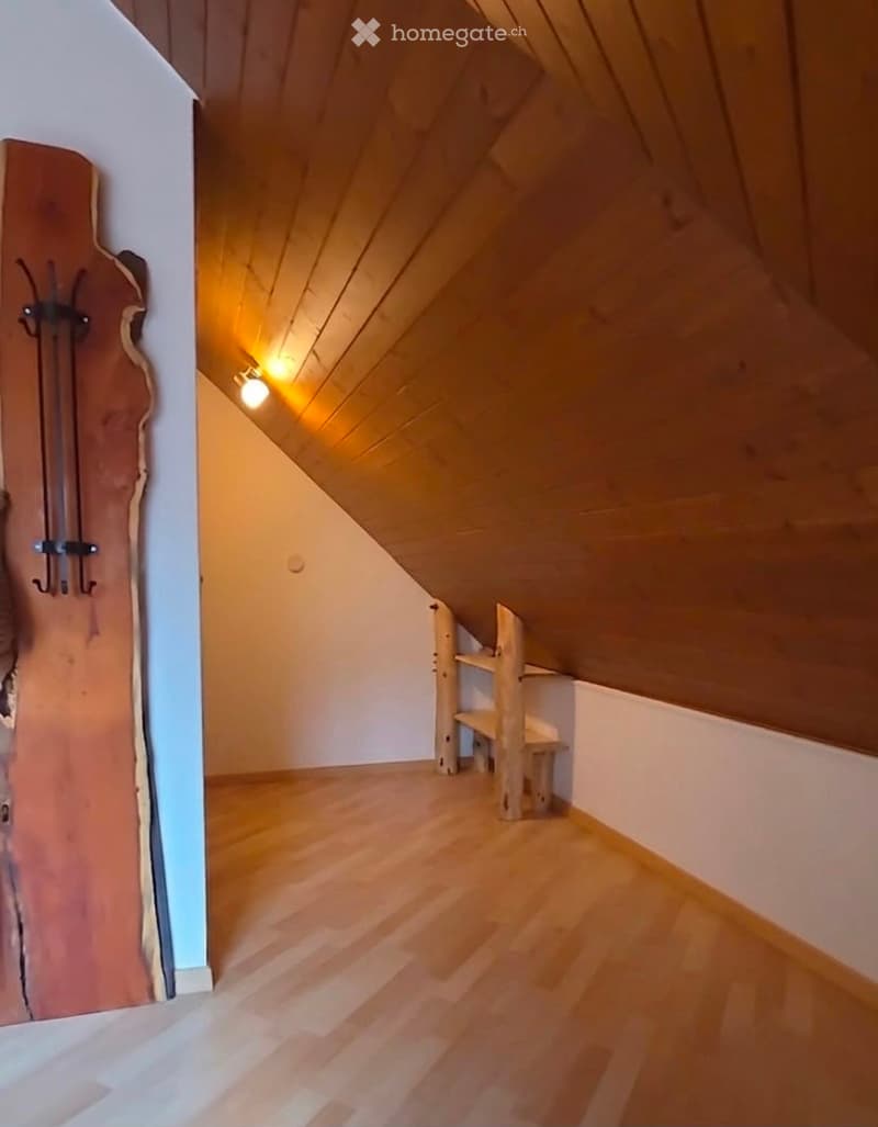 Empty attic room with wooden floors, slanted wooden ceiling, and built-in wooden shelving unit.