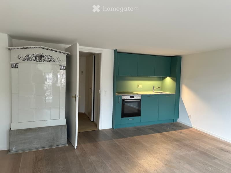Modern kitchen with teal cabinets, a built-in oven, and a sink with a faucet. The room features wooden flooring and an open doorway leading to another space.