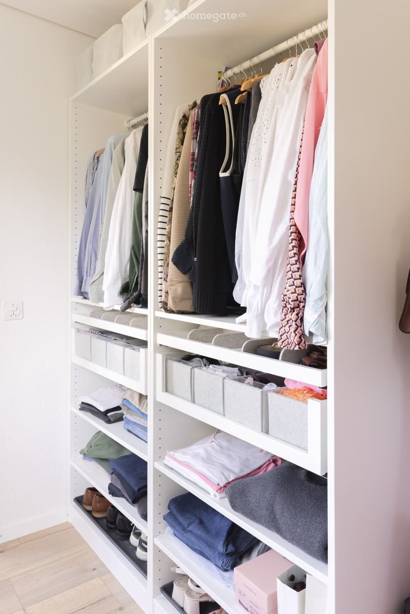 A well-organized walk-in closet with white shelving units, neatly arranged clothing, shoes, and storage boxes.