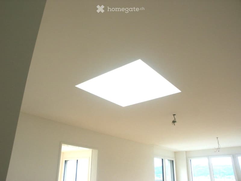 Empty room with beige walls, a large skylight, and windows showing a view of the sky and water.