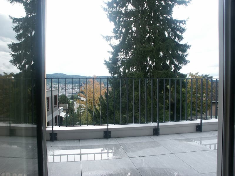 Balcony with tiled floor, metal railing, and scenic view of trees and cityscape.