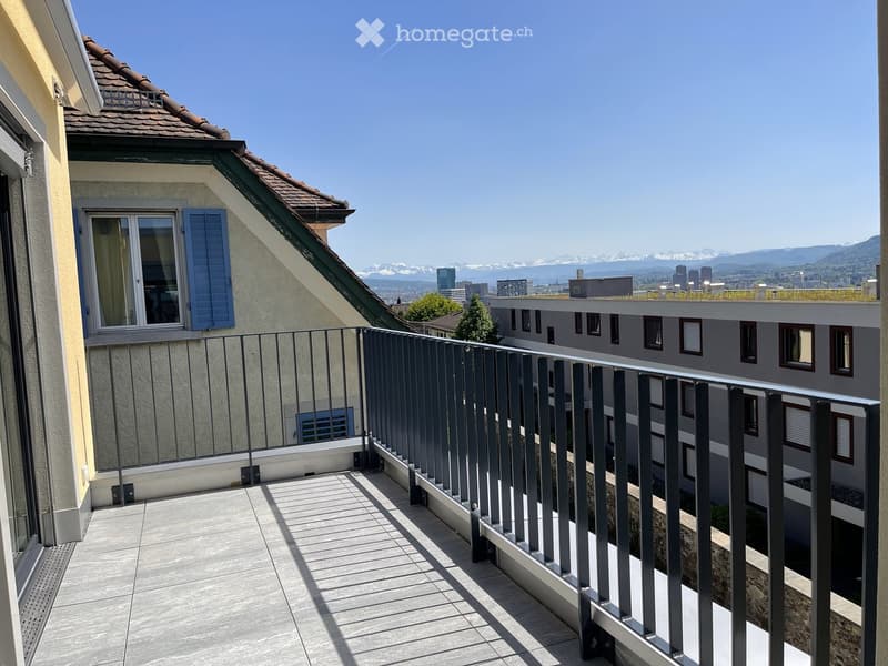 Balcony with modern metal railing, tiled floor, overlooking cityscape and mountains.