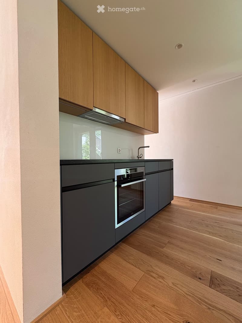 Modern kitchen with wooden and dark grey cabinets, stainless steel oven, and a sleek faucet on the countertop.