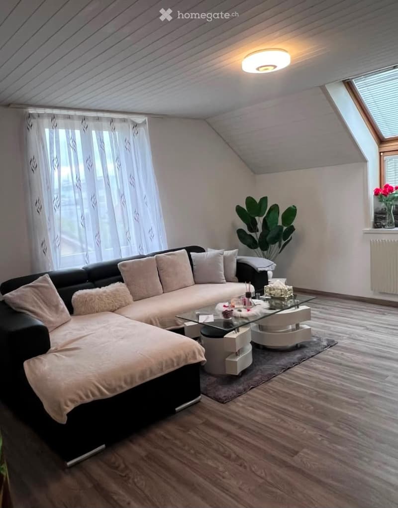Modern living room with a black sectional sofa, glass coffee table, floor lamp, and large window with white curtains.