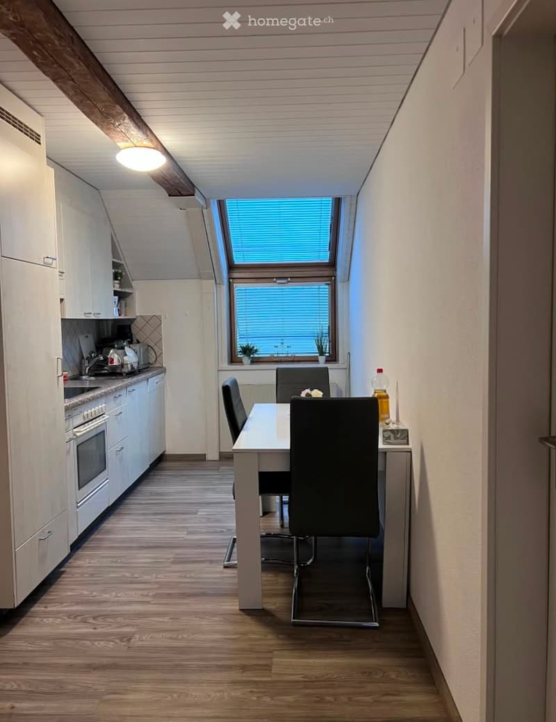 Modern kitchen and dining area with white cabinets, wooden flooring, and a large window with blinds. Includes a dining table with chairs, an oven, and a refrigerator.