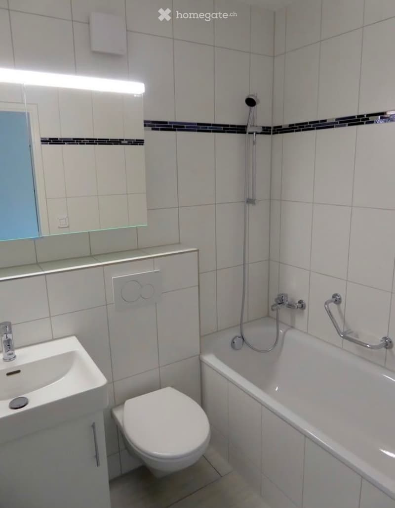 Modern bathroom with white tiles, a sink, toilet, bathtub, and a mirror above the sink.