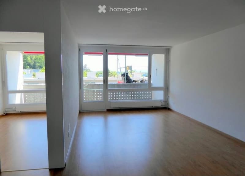 Empty room with wooden flooring, large windows, and a sliding glass door leading to a balcony.