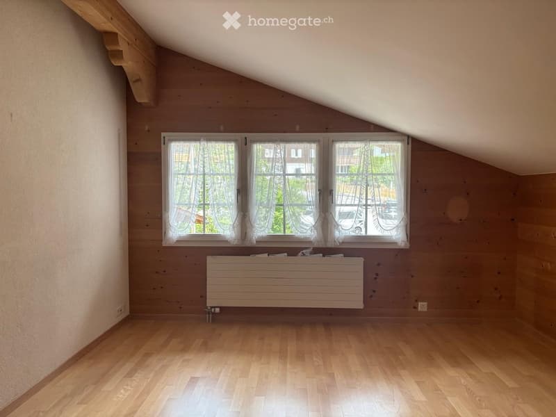 Empty attic room with wooden walls, wooden floor, large windows with white curtains, and a white radiator.