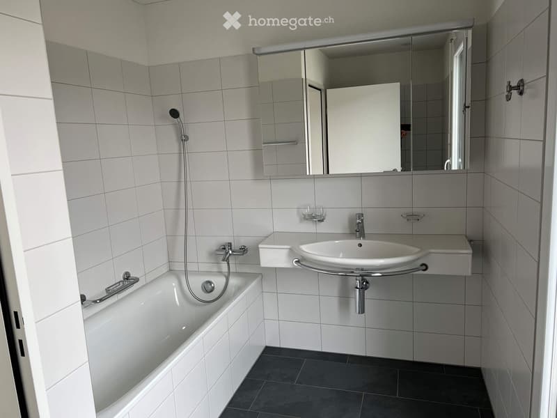 Modern bathroom with white tiled walls, a bathtub, a wall-mounted sink, a mirror, and a showerhead.