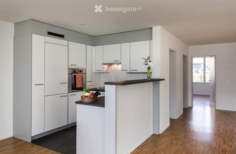 Modern kitchen with white cabinets, a black countertop, and a small island. A vase with flowers and a bowl of fruit are placed on the counter.