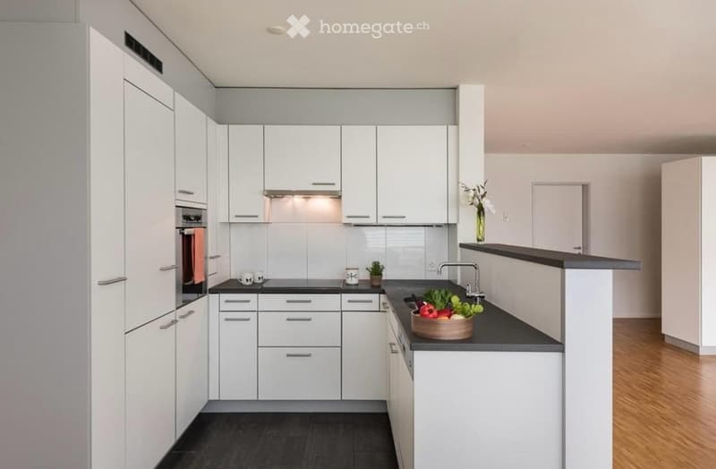 Modern kitchen with white cabinets, black countertops, and stainless steel appliances. Features a sink, faucet, and decorative bowl with vegetables on the counter.