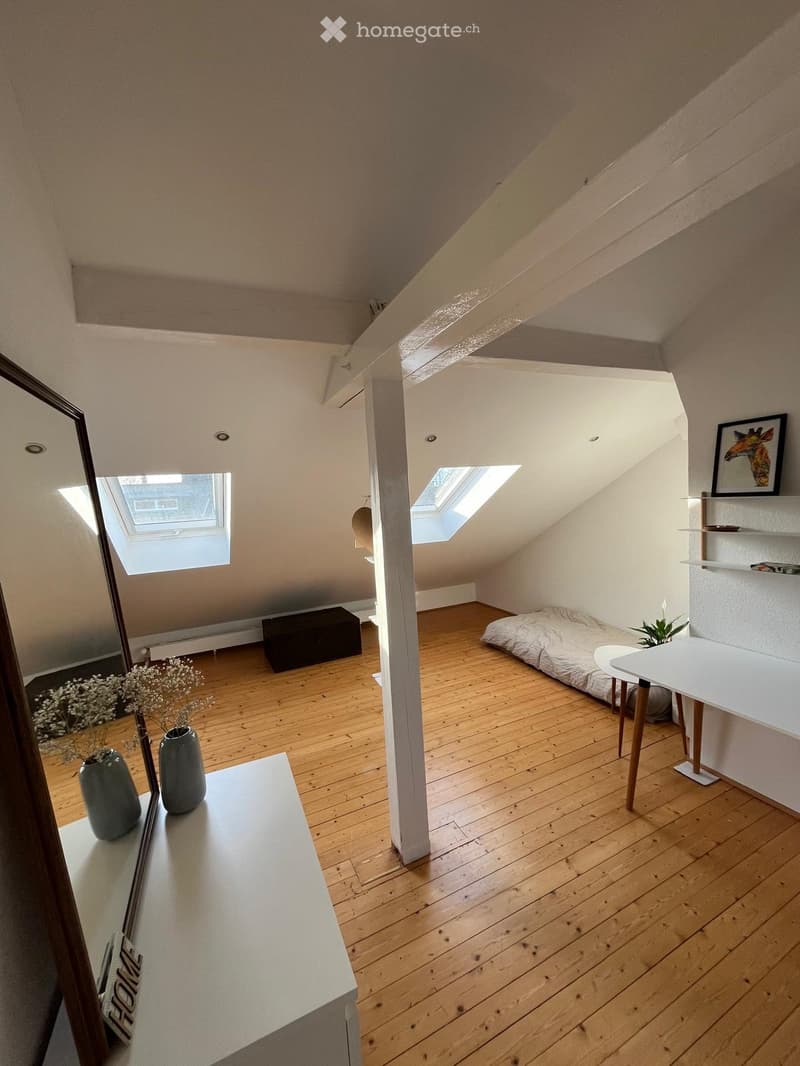 Loft-style room with wooden flooring, slanted ceilings, skylights, a small bed, a table with stools, shelves, and decorative vases.