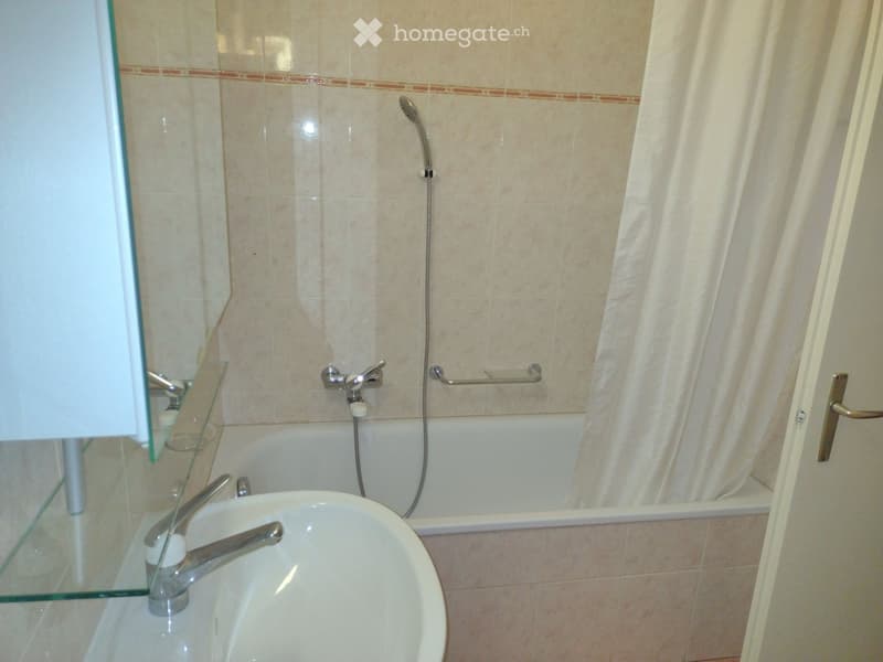 Bathroom with a white sink, bathtub, showerhead, and a glass cabinet with a mirror. Beige tiled walls and a white shower curtain.