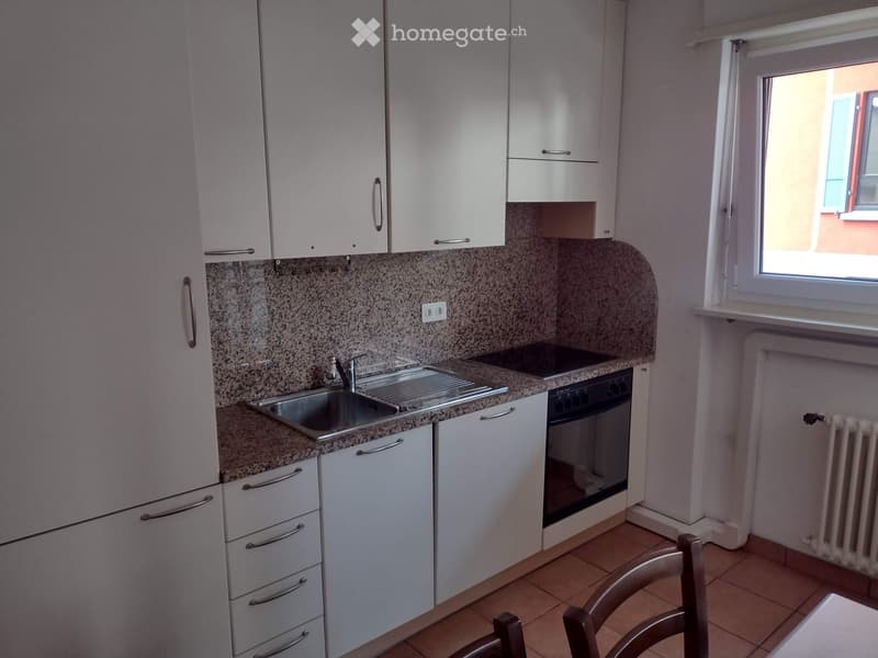 Modern kitchen with white cabinets, granite countertops, stainless steel sink, and built-in oven. Features a window with a view and a radiator below.