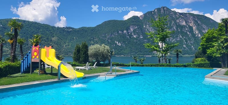 Outdoor area with a swimming pool, a water slide, lounge chairs, and a scenic mountain view in the background.