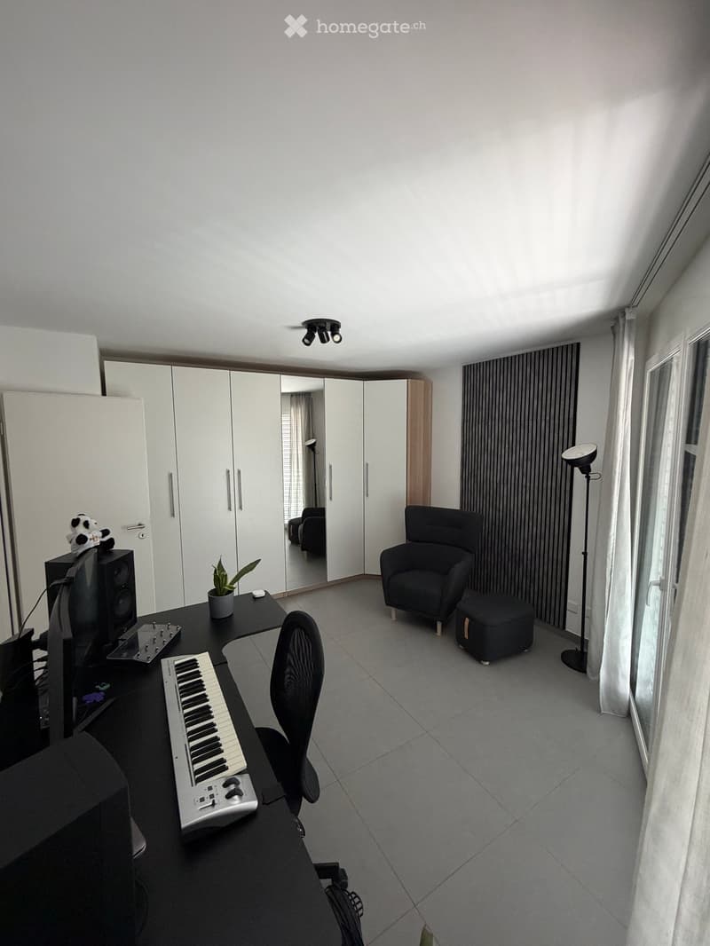 Modern, well-lit room with a desk, keyboard, chair, sofa, plant, mirror, wardrobe, and lamp.