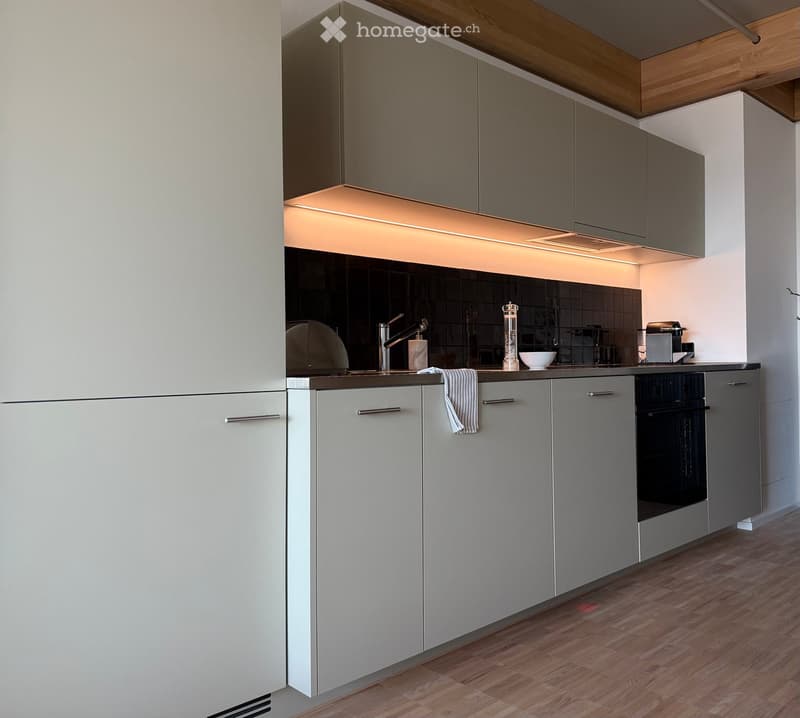 Modern kitchen with grey cabinets, wooden floor, and stainless steel appliances. Features a built-in oven, a sink with a modern faucet, and a countertop with a bowl and other small items.