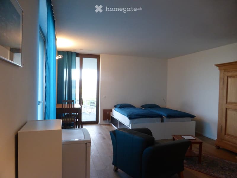 Brightly lit room with wooden flooring, two single beds, a sofa, a small table with chairs, and a wardrobe.