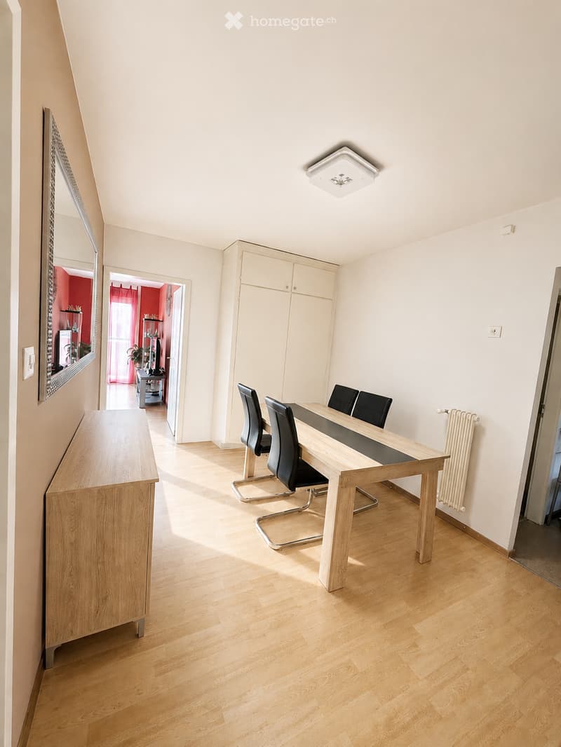 Bright dining room with wooden flooring, a modern dining table with four chairs, a tall wooden cabinet, and a large mirror on the wall.