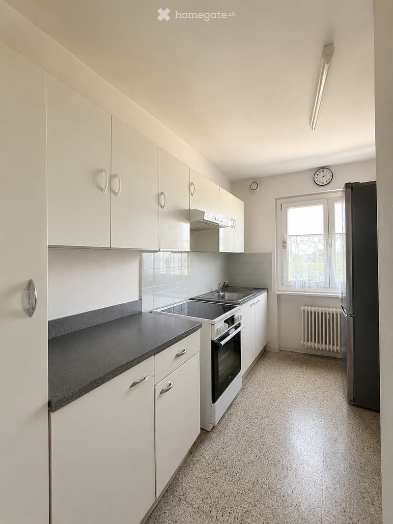 Modern kitchen with white cabinets, black countertop, stainless steel sink, oven, refrigerator, and radiator.