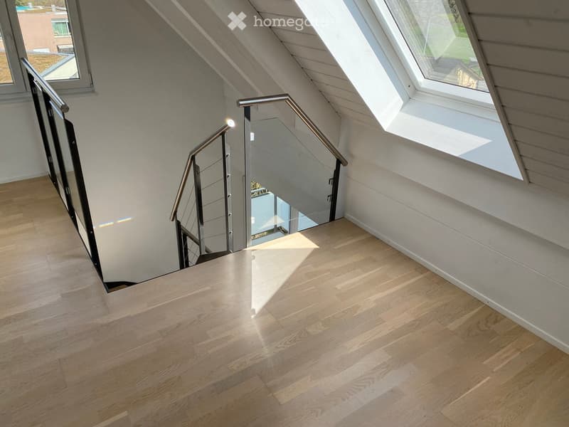 Modern hallway with light wooden flooring, sleek metal staircase railing, and skylight windows allowing natural light to flood the space.