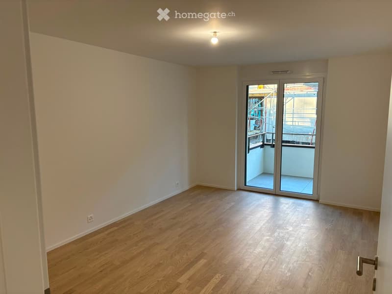 Empty room with wooden flooring, white walls, and a sliding glass door leading to a balcony.