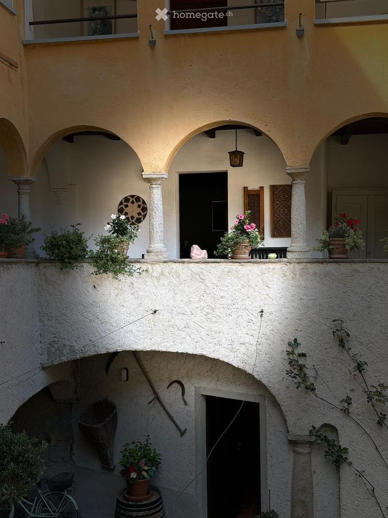 Balcony with arched columns, potted plants, a wicker basket, a bicycle, and a barrel.