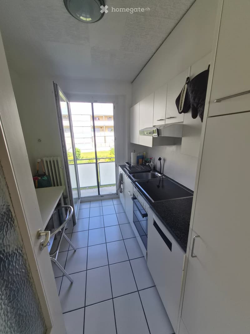Modern kitchen with white cabinets, black countertop, sink, and a sliding glass door leading to a balcony.
