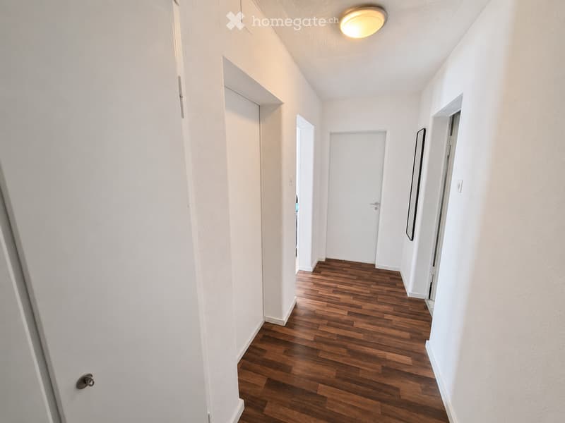 A narrow hallway with white walls, wooden flooring, and several doors leading to other rooms.