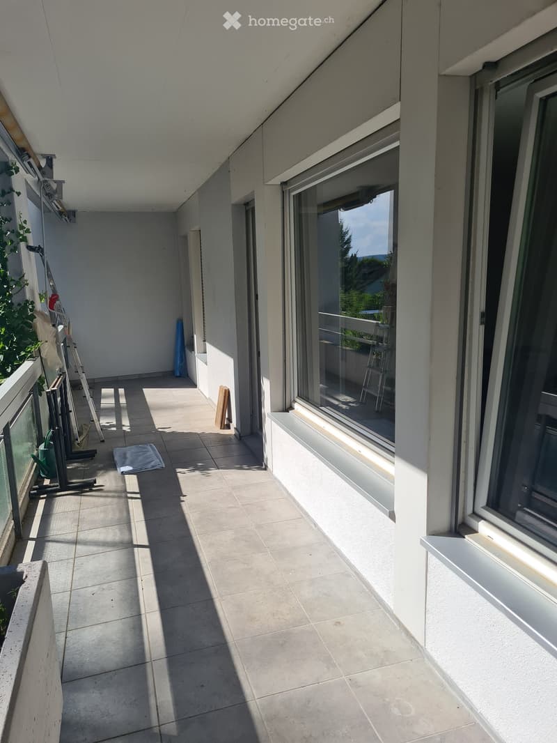 Balcony with tiled floor, white walls, large windows, and a view of greenery outside.