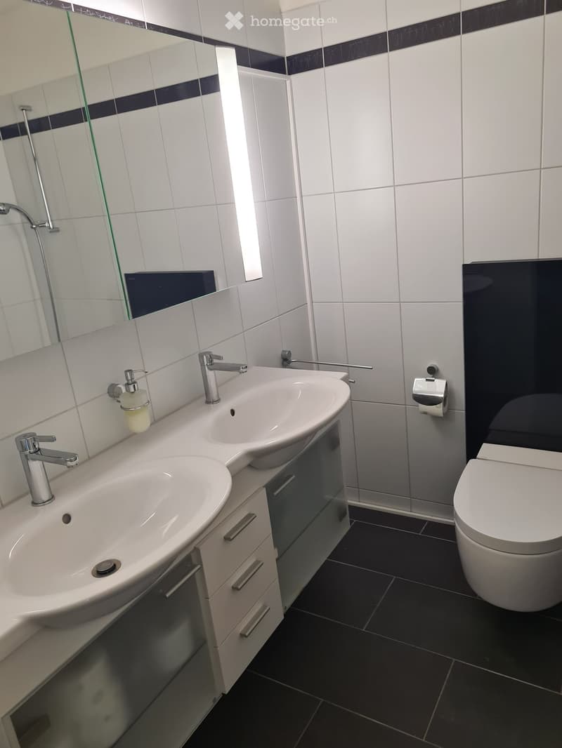 Modern bathroom with white tiles, black accents, double sink vanity, chrome faucets, and a toilet.