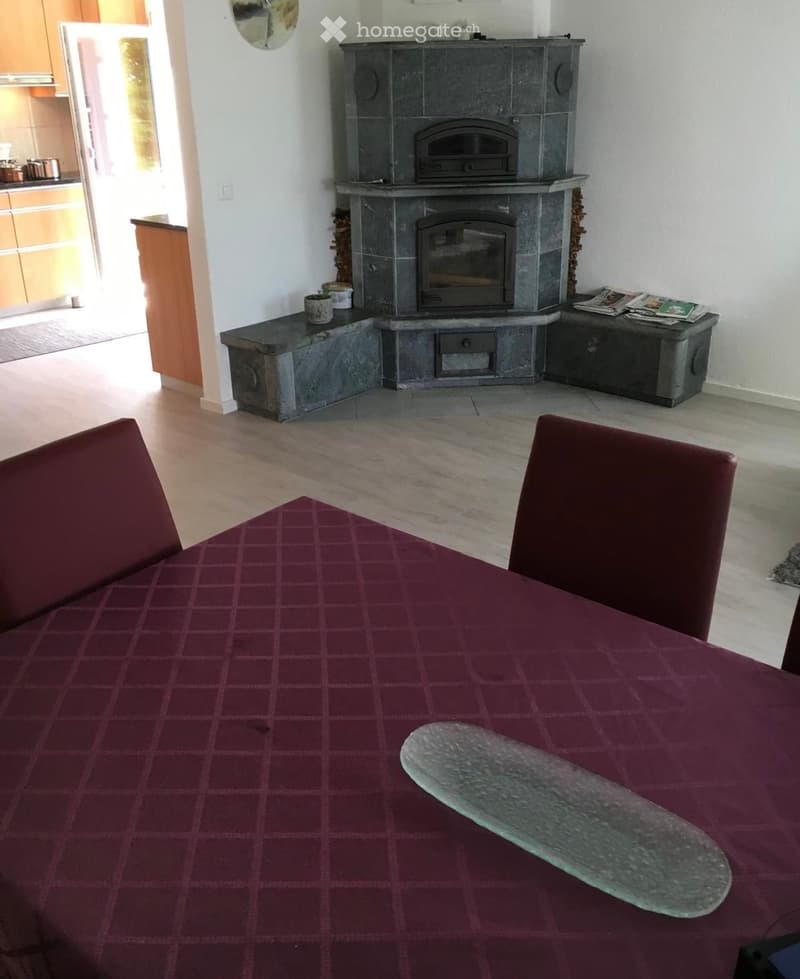 Dining area with a round table covered in a red checkered tablecloth, two red chairs, and a stone fireplace with a built-in oven and wood storage on either side.